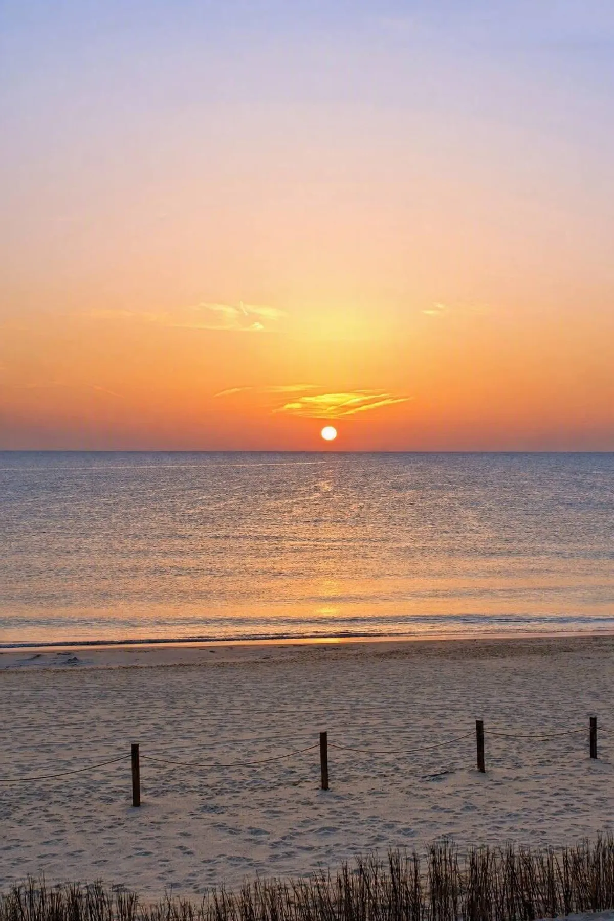 El sol asomando sobre el horizonte del Mediterráneo en la playa de la Llastra, con la arena y las dunas en primer plano
