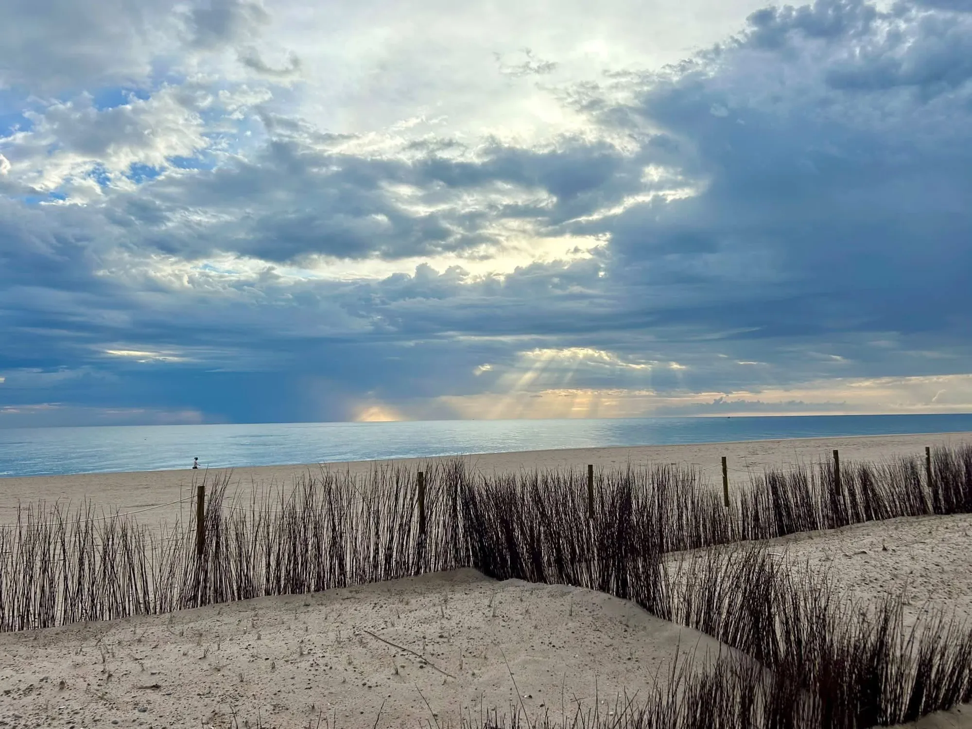 Dunas con vegetación y la playa de la Llastra bajo un cielo de nubes y rayos de sol