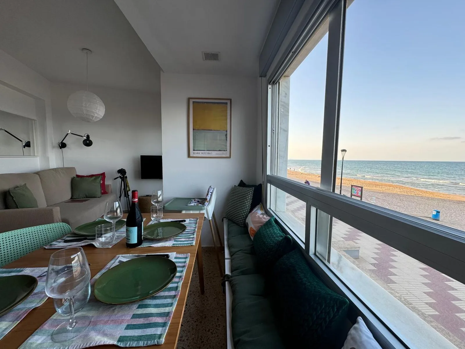 Salón-comedor del apartamento con la mesa junto al gran ventanal y vistas frontales a la playa de la Llastra y al mar Mediterráneo
