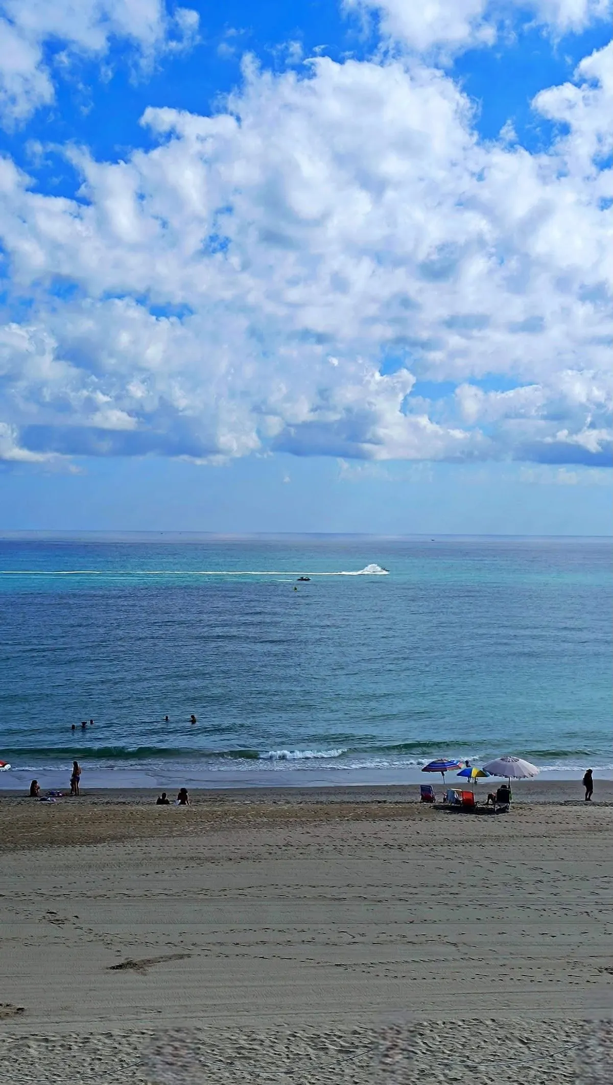 Día de verano en la playa de la Llastra visto desde el apartamento: arena, bañistas, sombrillas y mar turquesa